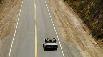 Movie still from “The Devil's Rejects” (2005), directed by Rob Zombie – A car driving down a road with a person in the back seat; Extreme Wide shot, High angle