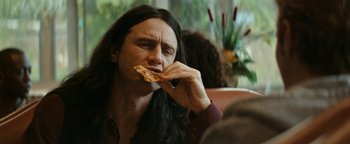 Movie still from “The Disaster Artist” (2017), directed by James Franco – A man with long black hair eating a piece of pizza; Close Up shot, Over the shoulder angle