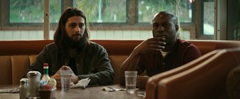 Movie still from “The Disaster Artist” (2017), directed by James Franco – Two men sitting at a table in front of a window; Medium shot, Low angle
