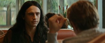 Movie still from “The Disaster Artist” (2017), directed by James Franco – A man sitting in front of another man in front of a window; Close Up shot, Over the shoulder angle
