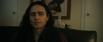 Movie still from “The Disaster Artist” (2017), directed by James Franco – A man with long black hair sitting on a couch; Close Up shot, Over the shoulder angle