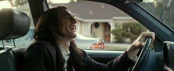 Movie still from “The Disaster Artist” (2017), directed by James Franco – A man sitting in a car with long black hair; Medium shot, Over the shoulder angle