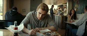 Movie still from “The Disaster Artist” (2017), directed by James Franco – A man sitting at a table writing on a piece of paper; Medium shot, High angle