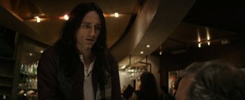 Movie still from “The Disaster Artist” (2017), directed by James Franco – A man with long black hair standing in a room; Close Up shot, Over the shoulder angle