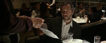 Movie still from “The Disaster Artist” (2017), directed by James Franco – A man sitting at a table in front of a glass of water; Medium shot, Over the shoulder angle