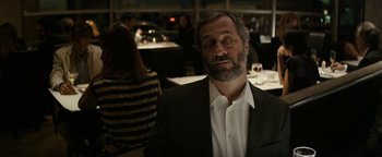 Movie still from “The Disaster Artist” (2017), directed by James Franco – A man with a beard and a suit is sitting at a table; Medium shot, Over the shoulder angle