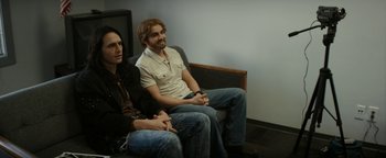 Movie still from “The Disaster Artist” (2017), directed by James Franco – Two men sitting on a couch in front of a tv; Medium shot, Over the shoulder angle