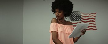 Movie still from “The Disaster Artist” (2017), directed by James Franco – A woman in a pink top is holding a tablet; Medium shot, Over the shoulder angle