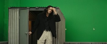 Movie still from “The Disaster Artist” (2017), directed by James Franco – A man with long black hair standing in front of a green wall; Medium shot, Over the shoulder angle