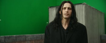 Movie still from “The Disaster Artist” (2017), directed by James Franco – A man with long black hair standing in front of a green wall; Medium shot, Over the shoulder angle