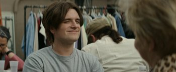 Movie still from “The Disaster Artist” (2017), directed by James Franco – A man with long brown hair smiles at the camera; Close Up shot, Over the shoulder angle