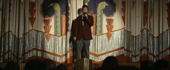 Movie still from “The Disaster Artist” (2017), directed by James Franco – A man standing on a stage holding a microphone; Wide shot, Low angle