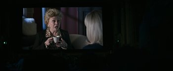 Movie still from “The Disaster Artist” (2017), directed by James Franco – An older woman holding a coffee cup in front of a television; Medium shot, Over the shoulder angle