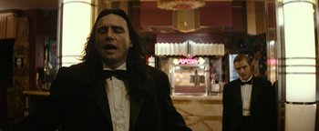 Movie still from “The Disaster Artist” (2017), directed by James Franco – A man with long black hair wearing a black tuxedo; Medium shot, Low angle