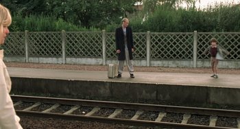 Movie still from “The Diving Bell and the Butterfly” (2007), directed by Julian Schnabel – A man in a suit is standing on the train tracks with a suitcase; Wide shot, High angle