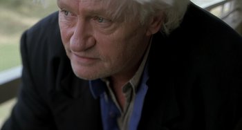 Movie still from “The Diving Bell and the Butterfly” (2007), directed by Julian Schnabel – An older man wearing a black jacket and a blue shirt; Close Up shot, Low angle