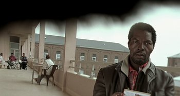 Movie still from “The Diving Bell and the Butterfly” (2007), directed by Julian Schnabel – A man sitting on top of a balcony next to a building; Close Up shot, Low angle