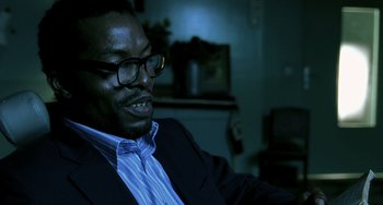 Movie still from “The Diving Bell and the Butterfly” (2007), directed by Julian Schnabel – A man in a suit and glasses is sitting in a room; Close Up shot, High angle