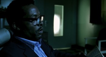 Movie still from “The Diving Bell and the Butterfly” (2007), directed by Julian Schnabel – A man in a suit and glasses is sitting in a dark room; Close Up shot, Low angle