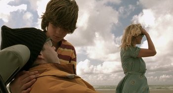 Movie still from “The Diving Bell and the Butterfly” (2007), directed by Julian Schnabel – A young boy holding a cell phone while standing next to a woman; Medium shot, Over the shoulder angle