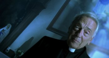 Movie still from “The Diving Bell and the Butterfly” (2007), directed by Julian Schnabel – An older man wearing a priest's collar; Close Up shot, Low angle
