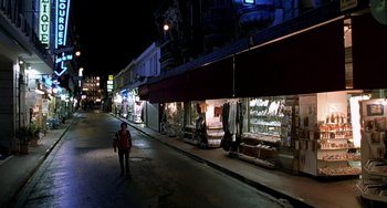 Movie still from “The Diving Bell and the Butterfly” (2007), directed by Julian Schnabel – A man walking down the street in front of a store at night; Extreme Wide shot, High angle