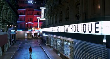 Movie still from “The Diving Bell and the Butterfly” (2007), directed by Julian Schnabel – A man walking down a street at night with neon lights; Extreme Wide shot, High angle