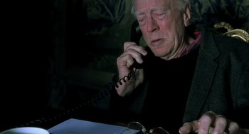Movie still from “The Diving Bell and the Butterfly” (2007), directed by Julian Schnabel – An older man talking on a phone while sitting at a table; Close Up shot, High angle