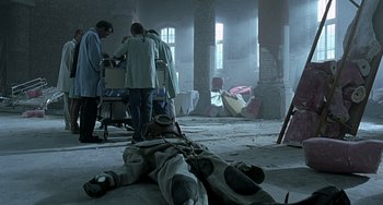 Movie still from “The Diving Bell and the Butterfly” (2007), directed by Julian Schnabel – A group of people standing in a room with a dead body laying on the ground; Wide shot, High angle