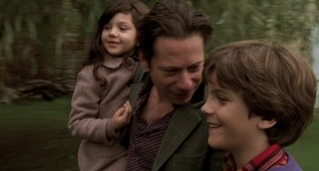 Movie still from “The Diving Bell and the Butterfly” (2007), directed by Julian Schnabel – A man and two children smiling for the camera; Close Up shot, Over the shoulder angle