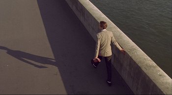Movie still from “The Dreamers” (2003), directed by Bernardo Bertolucci – A person walking on a bridge near a body of water; Wide shot, Overhead angle