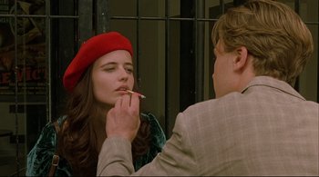 Movie still from “The Dreamers” (2003), directed by Bernardo Bertolucci – A woman in a red hat is putting a cigarette in her mouth while a man in a tan suit looks on; Close Up shot, Over the shoulder angle