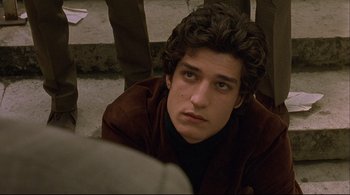 Movie still from “The Dreamers” (2003), directed by Bernardo Bertolucci – A young man sitting on the ground looking at the camera; Close Up shot, High angle
