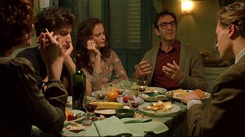 Movie still from “The Dreamers” (2003), directed by Bernardo Bertolucci – A group of people sitting at a table with plates of food; Medium shot, Over the shoulder angle