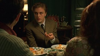 Movie still from “The Dreamers” (2003), directed by Bernardo Bertolucci – A man in a suit sitting in front of a plate of food; Medium shot, Over the shoulder angle