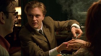 Movie still from “The Dreamers” (2003), directed by Bernardo Bertolucci – A man in a suit and tie holding a pair of cigarette lighters; Medium shot, Over the shoulder angle