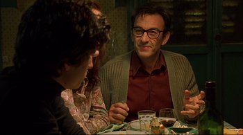 Movie still from “The Dreamers” (2003), directed by Bernardo Bertolucci – A man sitting at a table with two other people; Medium shot, Over the shoulder angle