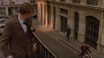 Movie still from “The Dreamers” (2003), directed by Bernardo Bertolucci – A man walking down a street while a woman is walking down the sidewalk; Wide shot, Over the shoulder angle