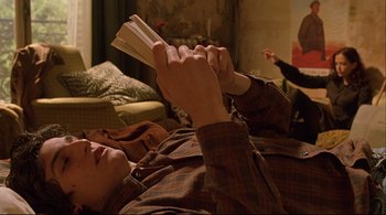 Movie still from “The Dreamers” (2003), directed by Bernardo Bertolucci – A man laying on the ground reading a book; Medium shot, Over the shoulder angle