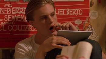 Movie still from “The Dreamers” (2003), directed by Bernardo Bertolucci – A young man is eating something while holding a book; Close Up shot, High angle