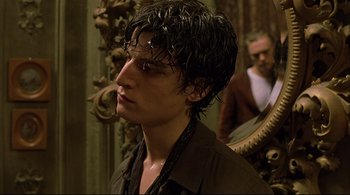 Movie still from “The Dreamers” (2003), directed by Bernardo Bertolucci – A young man with long black hair wearing a brown shirt; Close Up shot, Over the shoulder angle
