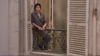 Movie still from “The Dreamers” (2003), directed by Bernardo Bertolucci – A man sitting on a balcony looking out of the window; Medium shot, Low angle