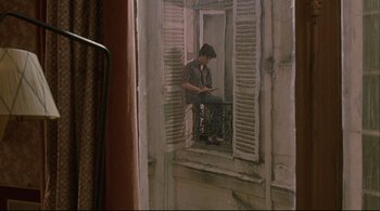 Movie still from “The Dreamers” (2003), directed by Bernardo Bertolucci – A man sitting on a window ledge looking out of a window; Wide shot, High angle