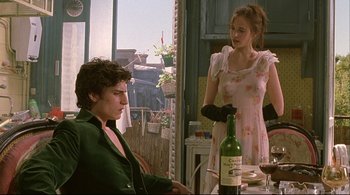 Movie still from “The Dreamers” (2003), directed by Bernardo Bertolucci – A man and a woman standing next to each other in front of a bottle of wine; Medium shot, Over the shoulder angle
