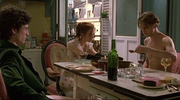 Movie still from “The Dreamers” (2003), directed by Bernardo Bertolucci – A woman sitting at a table with a wine glass; Medium shot, Over the shoulder angle