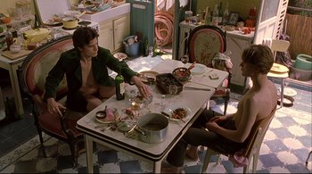 Movie still from “The Dreamers” (2003), directed by Bernardo Bertolucci – A group of people sitting around a table in a cluttered kitchen; Wide shot, High angle