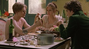 Movie still from “The Dreamers” (2003), directed by Bernardo Bertolucci – A group of people sitting around a table with food; Medium shot, High angle