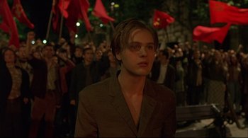 Movie still from “The Dreamers” (2003), directed by Bernardo Bertolucci – A man in a brown suit standing in front of a crowd of onlookers; Medium shot, Over the shoulder angle