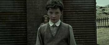 Movie still from “The Dressmaker” (2015), directed by Jocelyn Moorhouse – A young man standing in front of a brick wall with a young girl behind him; Medium shot, Low angle
