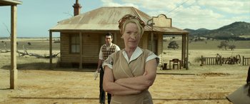 Movie still from “The Dressmaker” (2015), directed by Jocelyn Moorhouse – An older woman standing in front of an older man in front of an old house; Medium shot, Over the shoulder angle
